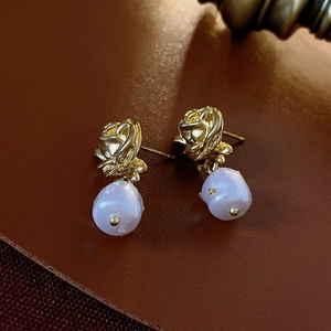 Macro shot of gold rose earrings with vintage baroque pearls on dark leather background