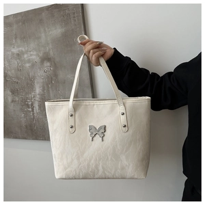 Close-up of white tote bag with ruched texture and silver butterfly metal detail