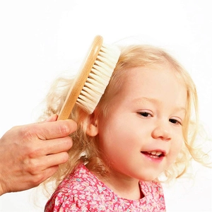 Close-up of a wooden baby brush with natural bristles grooming a child's golden hair