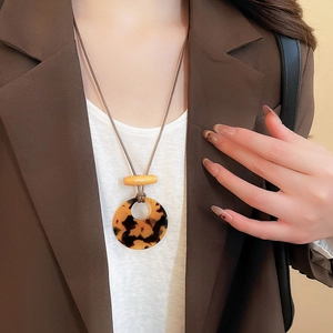 Detail of round tortoiseshell resin pendant with wood bar on brown cord worn by model