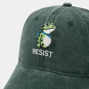 Detailed close-up of embroidered frog and RESIST text on washed cotton baseball cap
