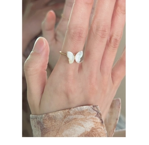 Detail of golden ring featuring white mother of pearl butterfly worn on finger