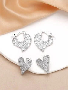 Flat lay of two pairs of silver heart-shaped earrings with zircon inlay on silk background