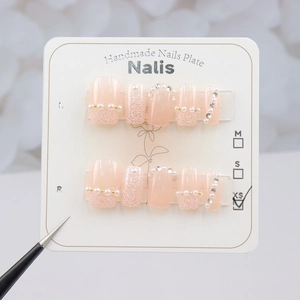 Detail of pink gradient press-on nails with pearls, fine glitter and XS size label