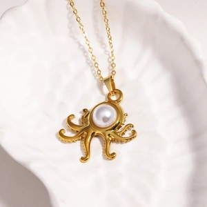 Vue macro du pendentif pieuvre dorée avec perle blanche sur un plateau coquillage