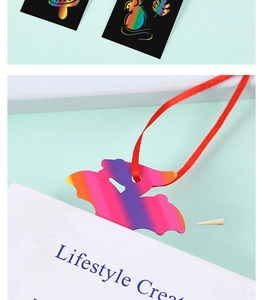 Detail showing bat-shaped rainbow scratch paper bookmark with wooden stylus and red ribbon