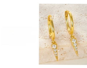 Detail of gold-plated hoop earrings with white zircon-inlaid triangle pendants on stone