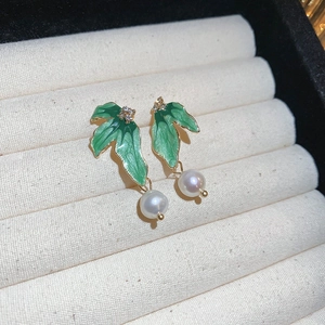 Macro shot of green leaf crystal earrings with pearls on a soft white display pad
