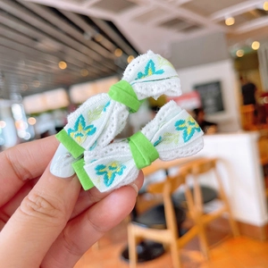 Detailed close-up of handmade embroidered flower bow hair clips in green and white color