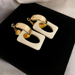 Detail of geometric resin earrings with gold metal rings on a black velvet display