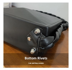 Close-up of bottom metal studs and braided handle on black matte leather bag