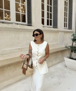 Détail d'un élégant gilet tricoté blanc avec boutons dorés dans un décor de rue extérieur