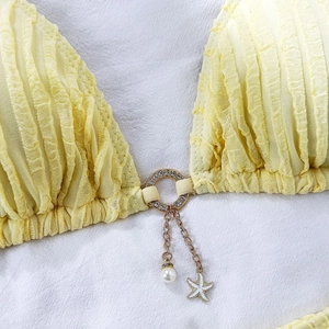 Close-up of bikini top featuring gold ring with pearl and starfish charms on yellow fabric