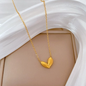 Detail of a golden sprout heart pendant on a thin O-chain over a beige jewelry box