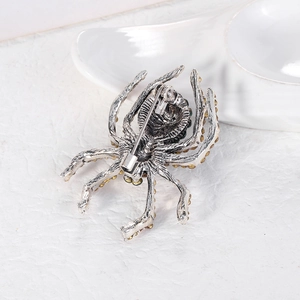 Vintage spider brooch in silver metal with green and yellow rhinestones on white surface