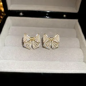 Elegant bow stud earrings with artificial pearls and crystals on a plush jewelry box display