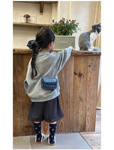 Detail of child's mini blue denim crossbody bag with frayed edges and silver chain strap