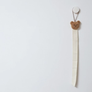 Hanging cotton strap hair accessory organizer with brown teddy bear on a white wall