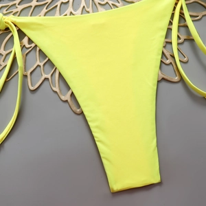 Detailed view of neon yellow tie-side bikini bottoms with textured fabric on a floral tray