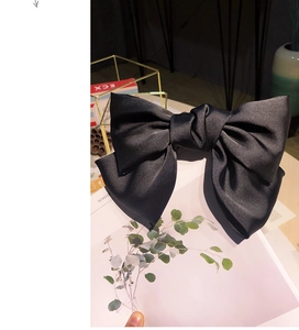 Detail of a large black satin bow hair clip on a decorative artistic background