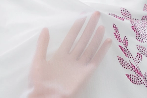 Detailed close-up of white mesh fabric with pink rhinestone leaf pattern and sheer texture