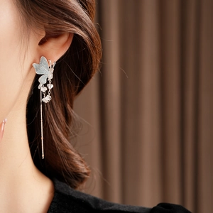 Détail de boucle d'oreille papillon argentée avec longues chaînes à glands sur modèle