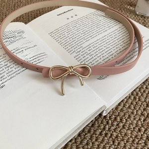 Detail of dusty pink leather belt with golden bow buckle on a vintage book