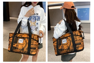 Detail view of large orange travel bag with black newspaper print and dual handle design