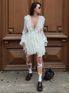 Detail of white chiffon mini dress featuring deep V-neck, lace-up front and ruffled hem