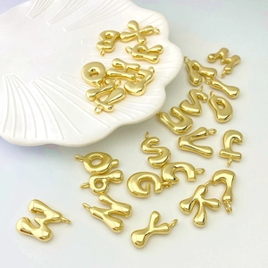 Fashionable gold puffed balloon letter pendants displayed on a white shell tray