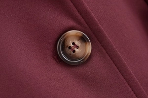 Gros plan détaillé d'un bouton en résine marron sur un tissu rouge foncé et coutures fines