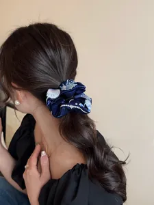 Close-up of navy blue embroidered scrunchie with silver shell patterns on a low ponytail