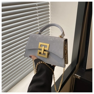 Close-up of grey suede shoulder bag with gold geometric buckle and chain strap