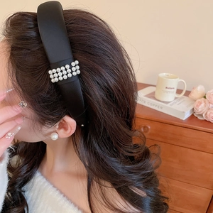 Detail view of the black satin padded headband with triple rows of white pearls on hair