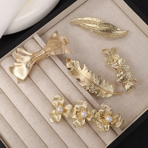 Collection of golden metal hair clips with leaf, feather and flower designs on tray