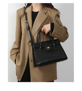 Fashionable black crocodile embossed handbag with gold hardware lock shown on model