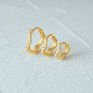 Detailed view of three gold-plated silver earrings with sparkling crystals in a wave design
