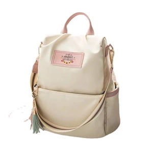 Cream white nylon backpack with pink leather accents and tassel charm in a studio view