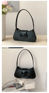 Close-up of glossy black baguette bag with bow detail on a wooden table and indoor setting