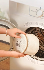Detailed view of hands placing a mesh bra laundry bag into a front-loading washing machine