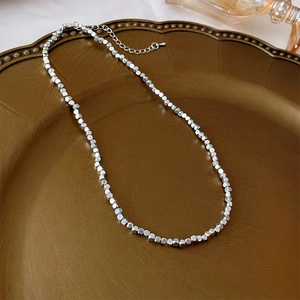 Macro shot of silver cube bead necklace on vintage gold plate showing metallic luster