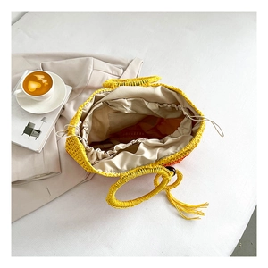 Detail of orange gradient straw tote bag with drawstring lining and tassel on white bedding