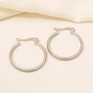 Detail of silver hoop earrings featuring horizontal textured lines and a secure latch clasp