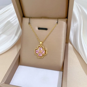 Detailed macro view of a gold four-leaf clover pendant with pink heart-shaped gems in a box
