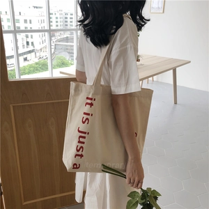 Minimalist beige canvas tote bag with red text print shown in a lifestyle street setting