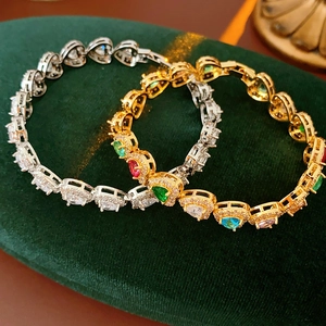 Macro shot of gold and silver bracelets with multicolored zircon stones on green velvet