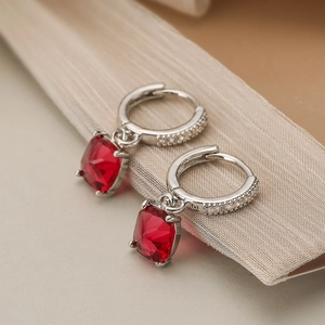 Close-up of geometric earrings with red square zircon drops on silver-plated copper base