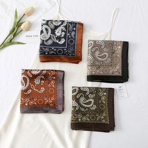 Detailed flat lay of paisley print square scarves in four colors on a white silk dress