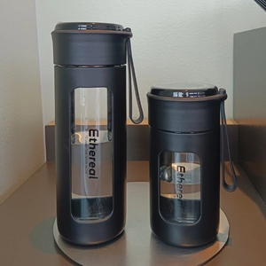 Detailed view of two minimalist portable glass water bottles with black matte sleeves