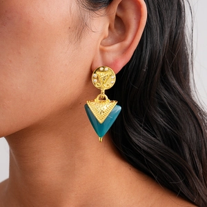 Gros plan détaillé d'une boucle d'oreille vintage dorée avec résine triangulaire sur modèle